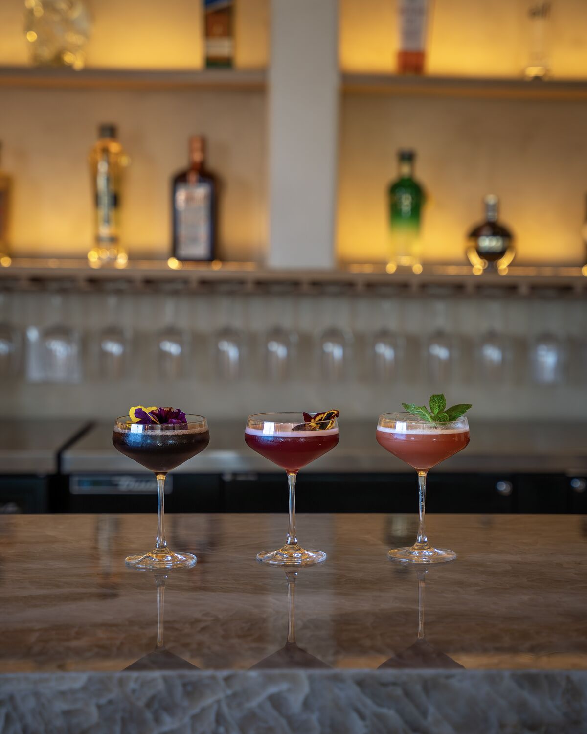 Three signature cocktails lined up on the marble bar in Manhattan Beach